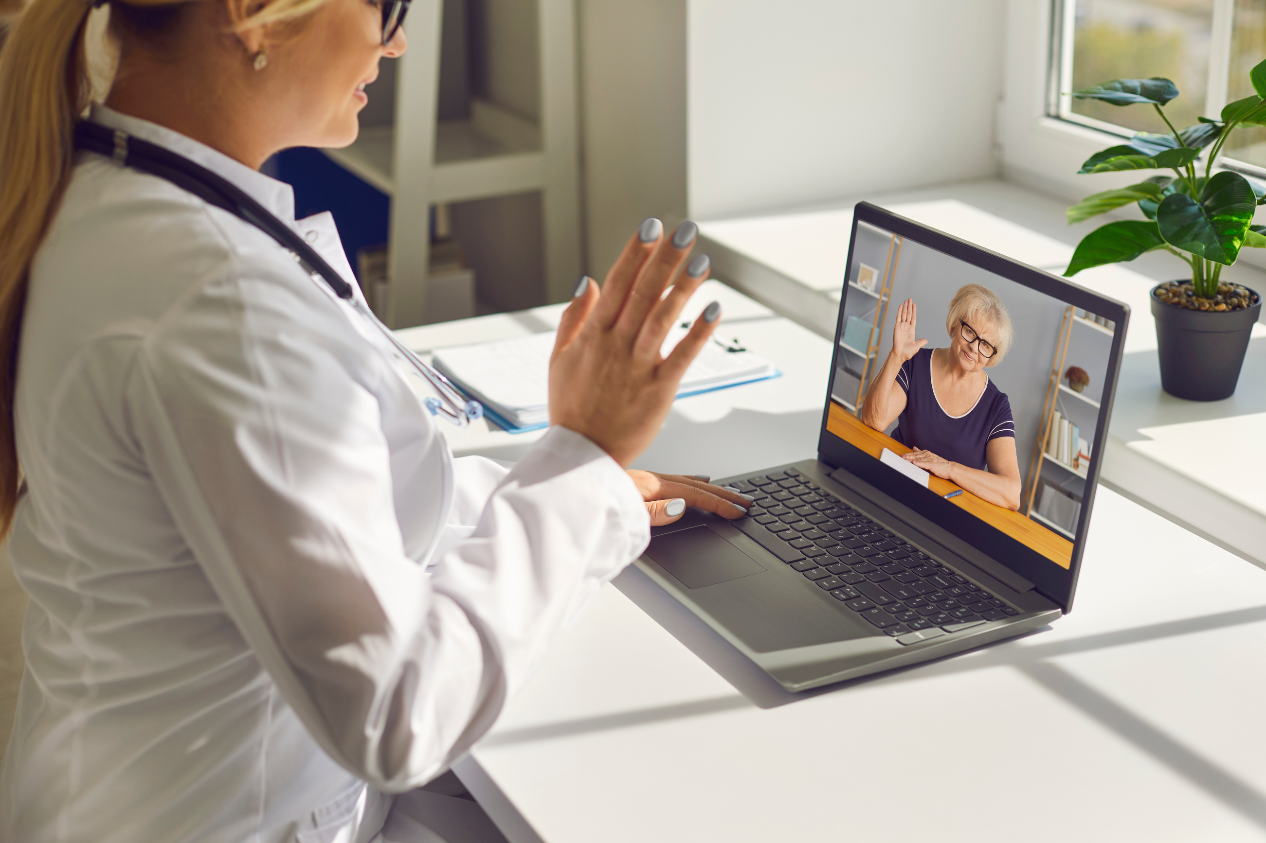 Doctor Waving Hand at Laptop Screen Saying Hello to Senior Woman during Online Consultation